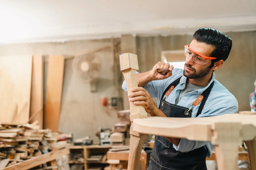 Young skilled carpenter crafting chair of wood